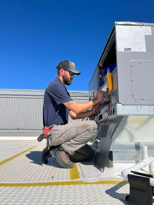 Technician taking readings on an ICP rooftop package unit against a blue sky