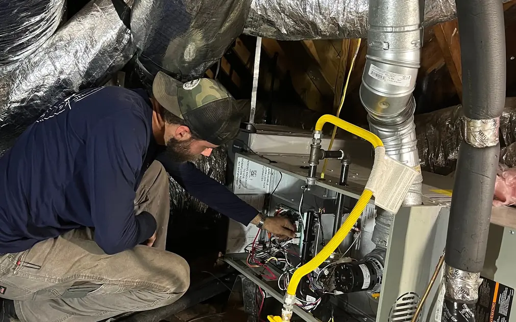 ASR technician at an attic gas furnace with the control board and gas flex in view