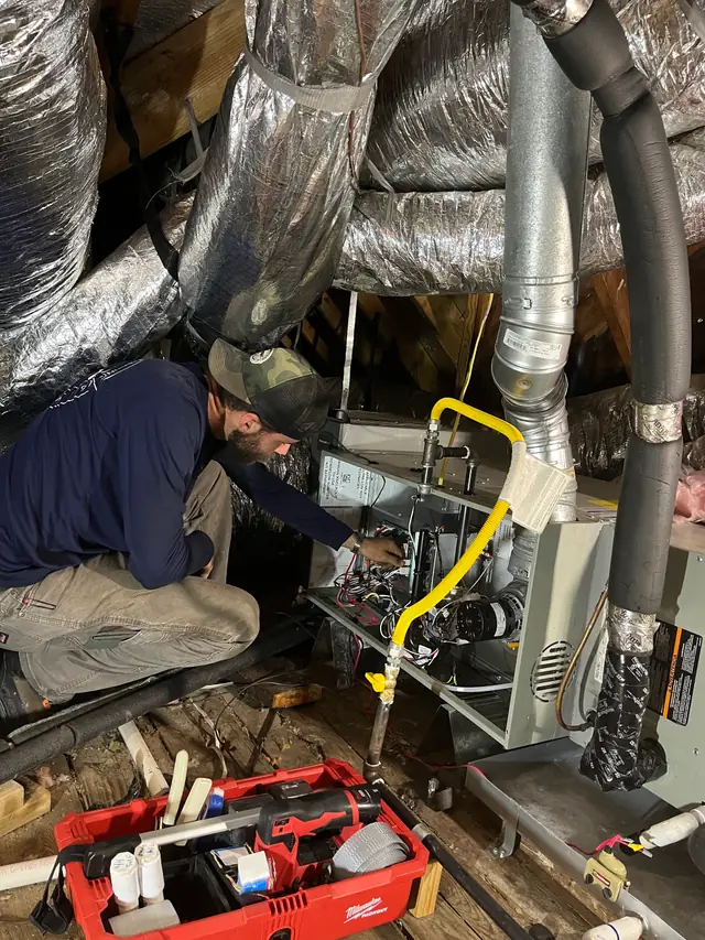 ASR technician working at an attic gas furnace with the service panel off